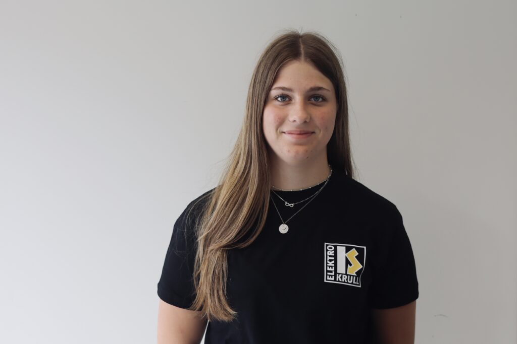 Mitarbeiterin der Krull Elektrotechnik GmbH im schwarzen Firmen-Shirt mit Logo, Porträt vor hellem Hintergrund